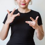 Mulher usa língua de sinais diante de um fundo neutro.