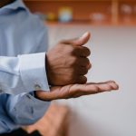 Homem se comunicando em língua de sinais em um ambiente interno, com foco nas mãos e na expressão durante a comunicação