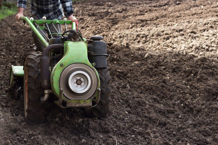 Agricultor opera um motocultivador em um campo recém-arado, preparando o solo para o plantio.