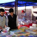 Pessoas folheiam livros em bancas de uma feira literária ao ar livre.