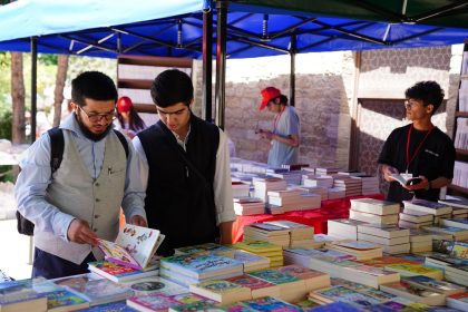 Pessoas folheiam livros em bancas de uma feira literária ao ar livre.
