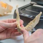Técnico refina um modelo dentário produzido em impressora 3D em um laboratório.