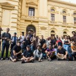 Grupo de fotógrafos reunido diante de um prédio histórico em um dia ensolarado