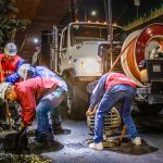 Trabalhadores realizam a limpeza de um sistema de drenagem urbana com máquinas, à noite, sob um viaduto.