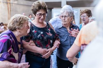 Mulheres idosas sorriem e conversam durante uma confraternização em ambiente interno.