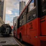 Ônibus urbano vermelho parado em um ponto moderno no centro de Curitiba.